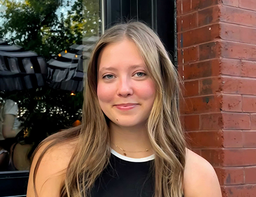 Jocelyn smiling standing in front of a window and brick wall